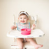 A giggling toddler girl sitting in her high chair with the pink Learning Bowl made from Silicone