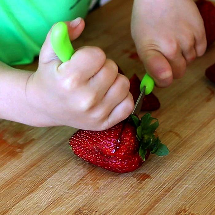 Little hand learning to cut a strawberry with the green Learning Cutlery Set