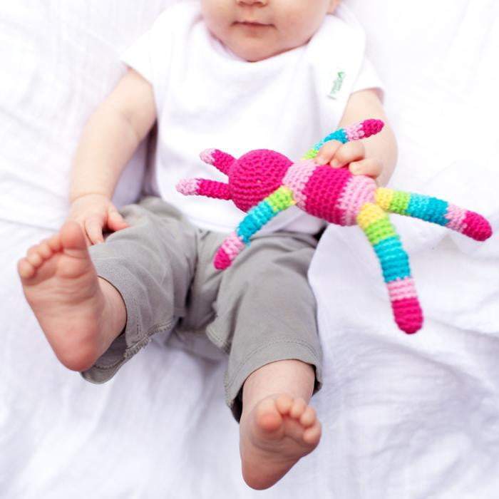 A tiny baby laying on a white pillow playing with the rabbit friend rattle.
