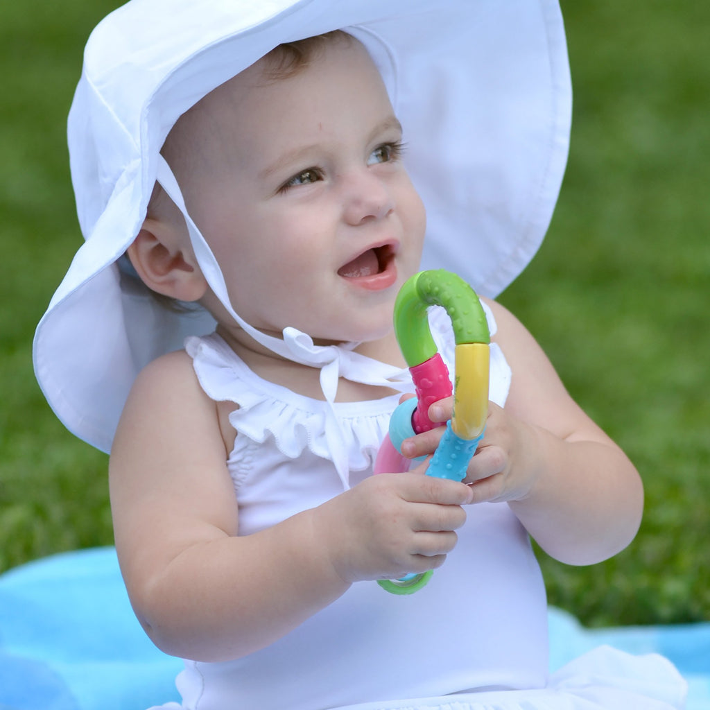A little girl smiling and playing with the Infinity Rattle while sitting outside