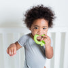 A cute little boy in a  white crib holding the green apple Fruit Teether made from Silicone in his mouth.