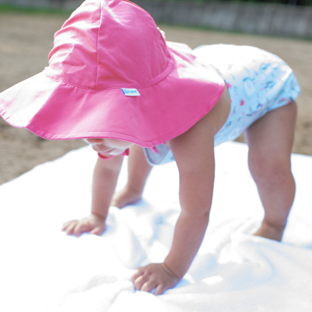 A toddler getting ready to stand up with the camera focused in on the hot pink Brim Sun Protection Hat.