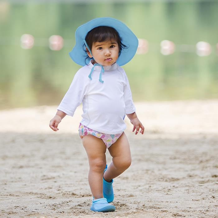 A little girl wearing a light blue Brim Sun Protection Hat while walking along the sand.
