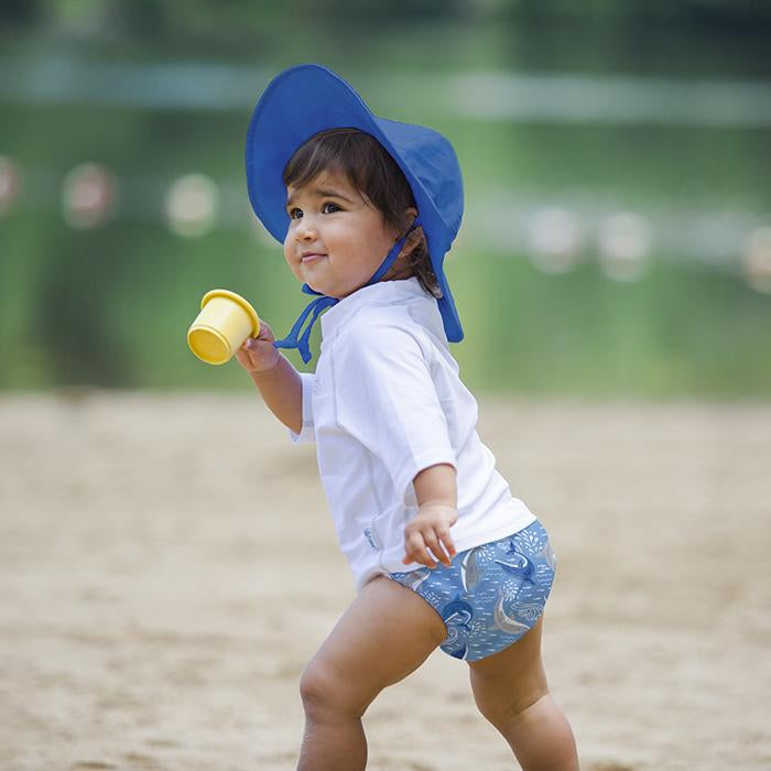 A young girl running with a yellow cup while wearing a royal blue Brim Sun Protection Hat.