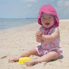 A cute happy little girl playing in the sand while being protected with her hot pink Flap Sun Protection Hat on.