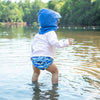 A little toddler boy waddling in the water while wearing the Royal Blue Flap Sun Protection Hat.