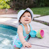 A cute little girl looking up from her pool with a big smile while wearing the white Breathable Swim and Sun Bucket Hat