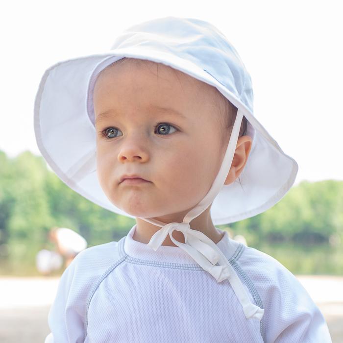 An up close view a toddler looking away from the camera with a white Bucket Sun Protection Hat on.