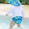 A young boy waddling in the shallow end of a pool while wearing Royal Blue Turtle Journey Bucket Sun Protection Hat and matching swim diaper.