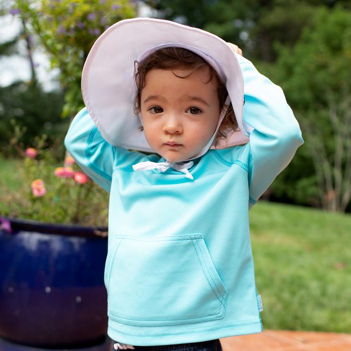 A toddler looking at the camera with her hands over her head while wearing the aqua Breathable Sun Protection Shirt.