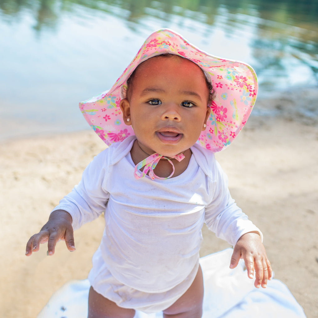 A pretty little baby girl with a Brim Sun Protection Hat on looking up into the camera.