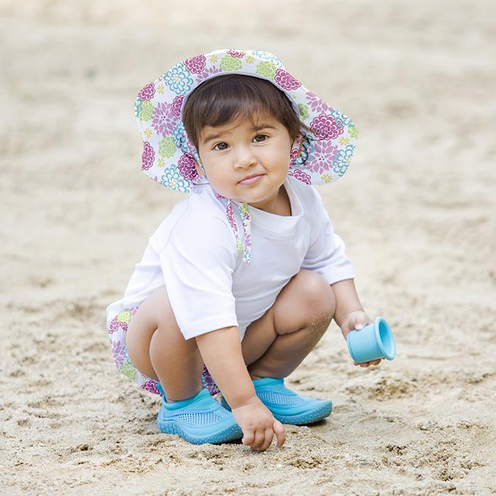 A cute young girl wearing Brim Sun Protection Hat while squatting and playing in the sand. She is looking at the viewer with a questionable smirk.