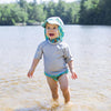 A young boy with a wide smile while looking up and standing in the shallow lake with a light aqua sea friends Flap Sun Protection Hat.