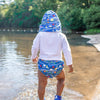 A little boy walking away along the lake shower and wearing his Royal Blue Sea Friends Flap Sun Protection Hat and swim diapers to match.